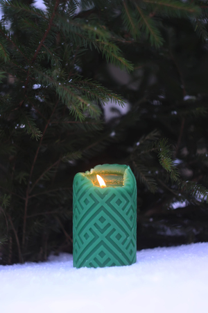 Green candle on the snow near the fir-tree outdoorsの写真素材