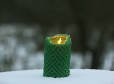 Green candle on the snow-covered tree stump outdoorsの写真素材