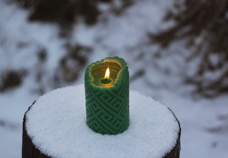 Green candle on the snow-covered tree stump outdoorsの写真素材
