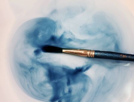 Brush with a blue watercolor paint in a cup of transparent waterの写真素材