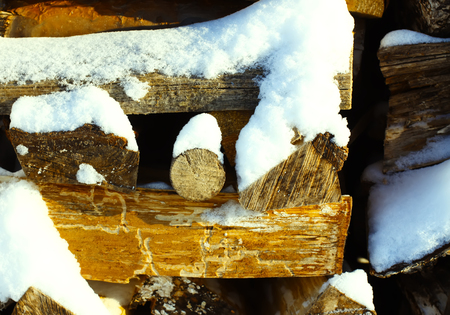 Stacked dry chopped firewood logs with snow.