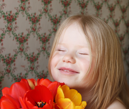 A little smiling girl with red and yellow tulip flowersの写真素材
