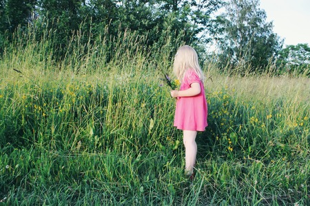 Adorable blonde little girl in a pink dress walking in the summer field in the countryside.の写真素材