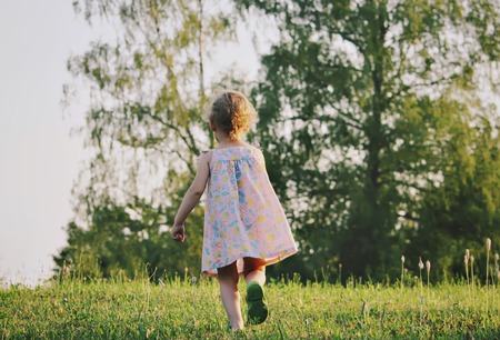 Adorable little girl running in the summer field in the countryside.の写真素材