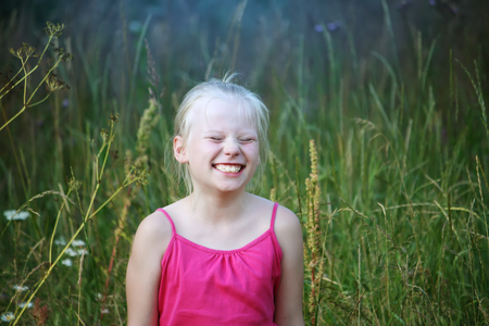 Adorable smiling blonde girl in bright dress in ethnic style walking in the green field at summer.の写真素材