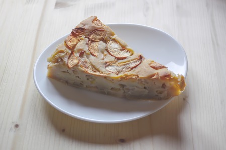 Homemade sweet apple pie with cinnamon and and powdered sugar on a white plate on light wood background.の写真素材