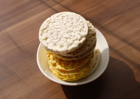 White and yellow flat round rice and corn crackers on wooden table background.