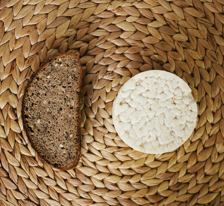 White flat round rice cracker and a piece of rye bread on whicker place mat background.