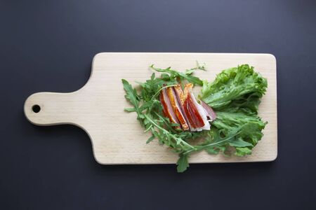 Sliced ham with fresh green lettuce and ruccola leaves on a cutting board.の写真素材