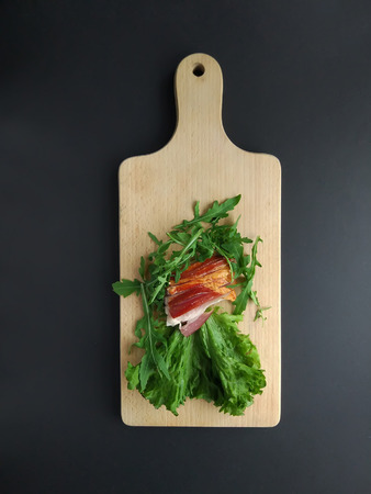 Sliced ham with fresh green lettuce and ruccola leaves on a cutting board.の写真素材