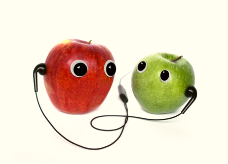 Red and green small apple with cute eyes and headphones on white background. Conceptual photo.の写真素材