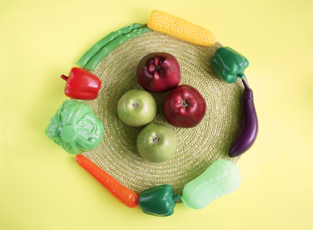 Fresh ripe red and green apples and artificial plastic vegetables in circle on wicker place mat. Conceptual photo.の写真素材