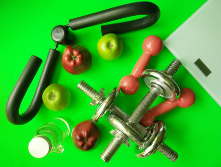 Set of different objects. Dumbbells, shoulder expander, electronic scales, water bottle and fresh apples on bright green background. Fitness and healthy nutrition concept.の写真素材