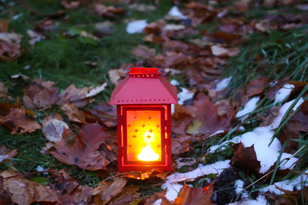 Decorative lantern with burning candle on fall leaves background in autumn park at evening.の写真素材