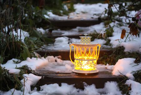 Decorative lantern with burning candle on old wooden stairs in winter park at evening.の写真素材