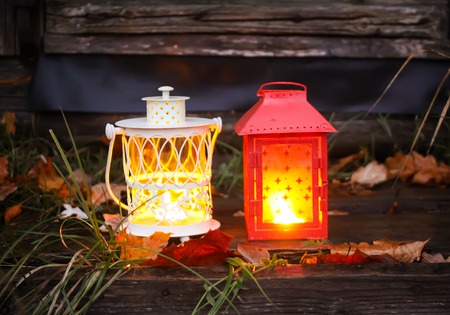 Decorative lanterns with burning candles on old wooden threshold of rural bathhouse in autumn park at evening.の写真素材