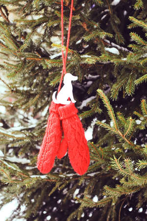 Red mittens with paper dog figure on fir tree green branches.