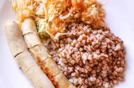 Buckwheat with fried sausages and fresh salad with raw carrots and cabbage.の写真素材