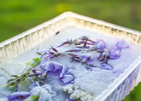 Ice cube with flowers on green grass at summer.
