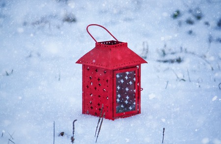 Red lantern with burning candle on fresh snow. Snowy winter evening in park.の写真素材