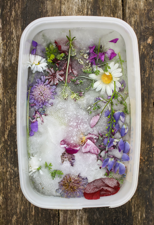 Ice cube with different summer flowers on green grass at summer.の写真素材