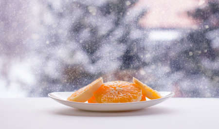 Sliced sweet ripe orange on a white plate on winter nature blurred background.の写真素材