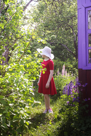 A girl in a hat and red dress walking in a small garden in the countryside at summer.の写真素材
