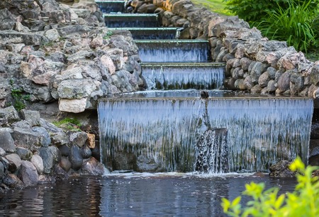 Cold transparent water of decorative artificial waterfall in summer park.
