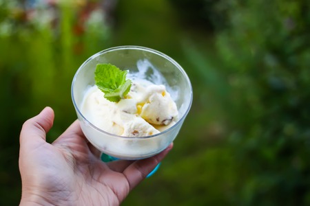 Icecream with fresh green mint leaves in a transparent vase in a hand on summer nature background.の写真素材