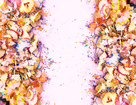 Wooden pencil shavings and colorful crumbs of graphite from sharpener on soft pink paper background. Top view. Symmetrical design with empty space for text for poster, banner, cards.の写真素材