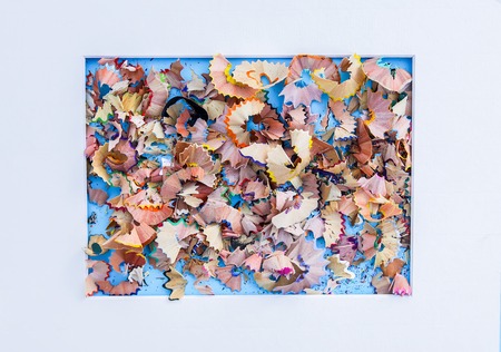 Wooden pencil shavings from sharpener on blue background in a white paper frame. Top viewの写真素材
