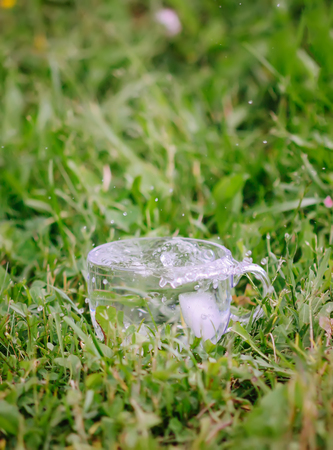 Splash of cool fresh water with ice cubes in the transparent glass cup outoors in summer day.の写真素材