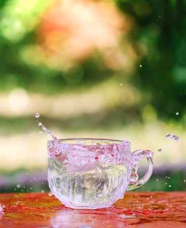 Splash of cool fresh water with ice cube in the transparent glass cup in the table outoors in summer day.の写真素材