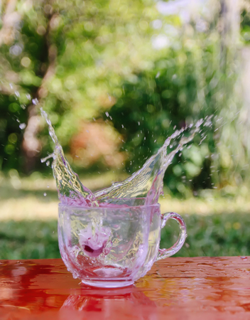Splash of cool fresh water with ice cube in the transparent glass cup in the table outoors in summer day.の写真素材