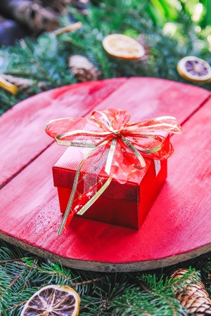 Christmas, New Year winter holiday composition with red wooden surface on green fir-tree branches, dried orange slices, cones , gift box and red bow.の写真素材