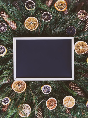 Empty framed board on green fir-tree branches decorated with dried orange slices and cones. Christmas, New Year winter holiday festive composition.の写真素材