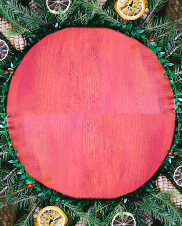 Christmas and New Year winter holiday composition with red wooden surface on green fir-tree branches, dried orange slices, conesの写真素材
