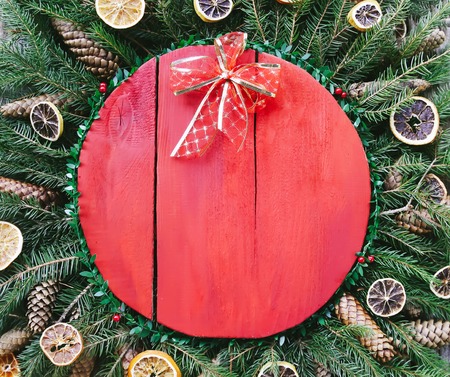 Christmas and New Year winter holiday composition with red wooden surface on green fir-tree branches, dried orange slices, cones and red bow.の写真素材
