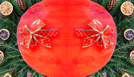 Christmas and New Year winter holiday composition with red wooden surface on green fir-tree branches, dried orange slices, cones and red bow.の写真素材