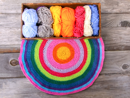 Knitted striped mat and colorful skeins of wollen yarn on wooden background.
