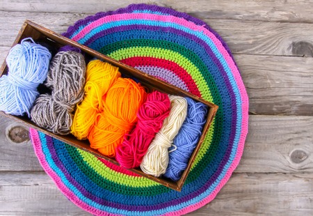 Knitted striped mat and colorful skeins of wollen yarn on wooden background.の写真素材