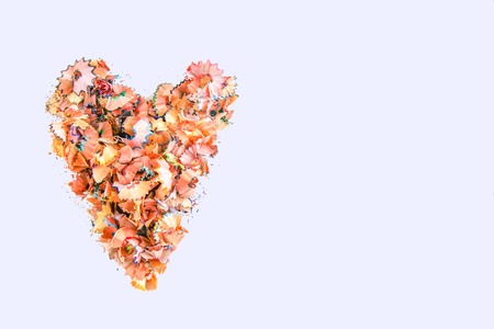 Wooden pencil shavings and colorful crumbs of graphite from sharpener in a shape of heart on white background. Top view. Design elements for poster, banner, cardsの写真素材