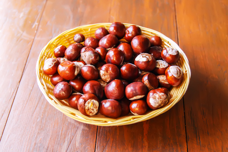 Fresh raw autumn chestnuts in a basket on wooden table. Aesculus hippocastanum.の写真素材