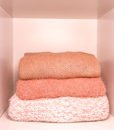 Pile of warm autumn and winter knitted sweaters on a home wardrobe shelf. Modern fashion clothes in shades of living coral.の写真素材