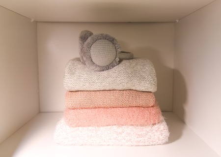 White shelf of the home wardrobe with colorful sweaters, jumpers and warm headphones. Small space organization, minimalism concept.の写真素材