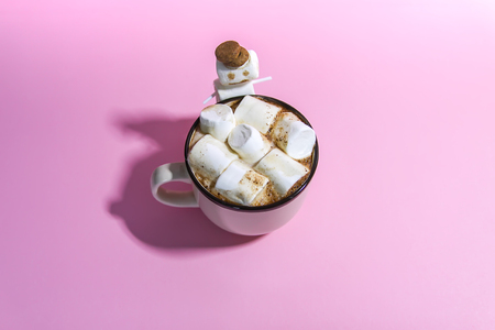 Ceramic mug with hot fresh cocoa drink and melted handmade funny marshmallow snowman on soft pink background.の写真素材