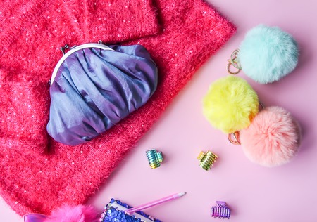 Bright composition of fashion accessories and dress. Glitter sequins sweetshot, purse, colorful pompons and hair bands. Different objects on soft pink pastel background. Flat lay, top view.の写真素材