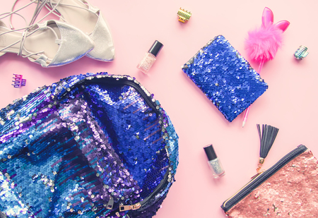 Bright composition of fashion accessories. Glitter sequins backpack, purse, funny pen, nail polish and hair elastic bands. Different objects on soft pastel background. Flat lay, top viewの写真素材