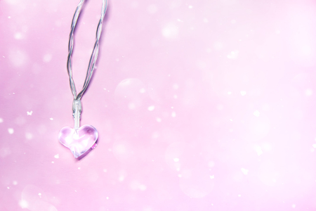 Small transparent glass heart on soft pink background with bokeh effect. Valentine's day symbol. Decorative element. Festive Valentine card.の写真素材