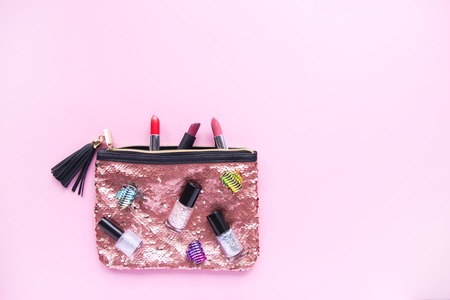 Bright composition of fashion accessories. Glitter sequins cosmetic bag with nail polishes, lipsticks, hair pins. Objects on soft pastel background. Flat lay, top viewの写真素材